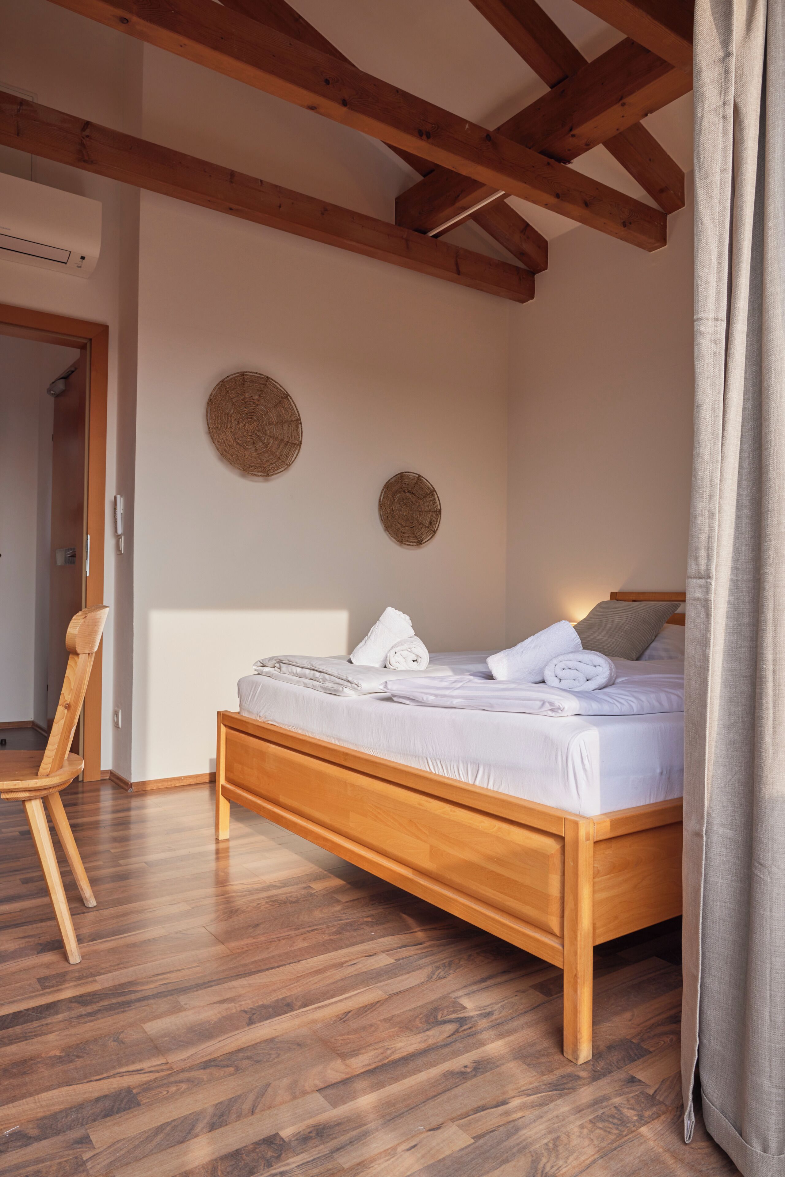 Een slaapkamer met een houten bed, een houten stoel en een plafond met zichtbare balken.