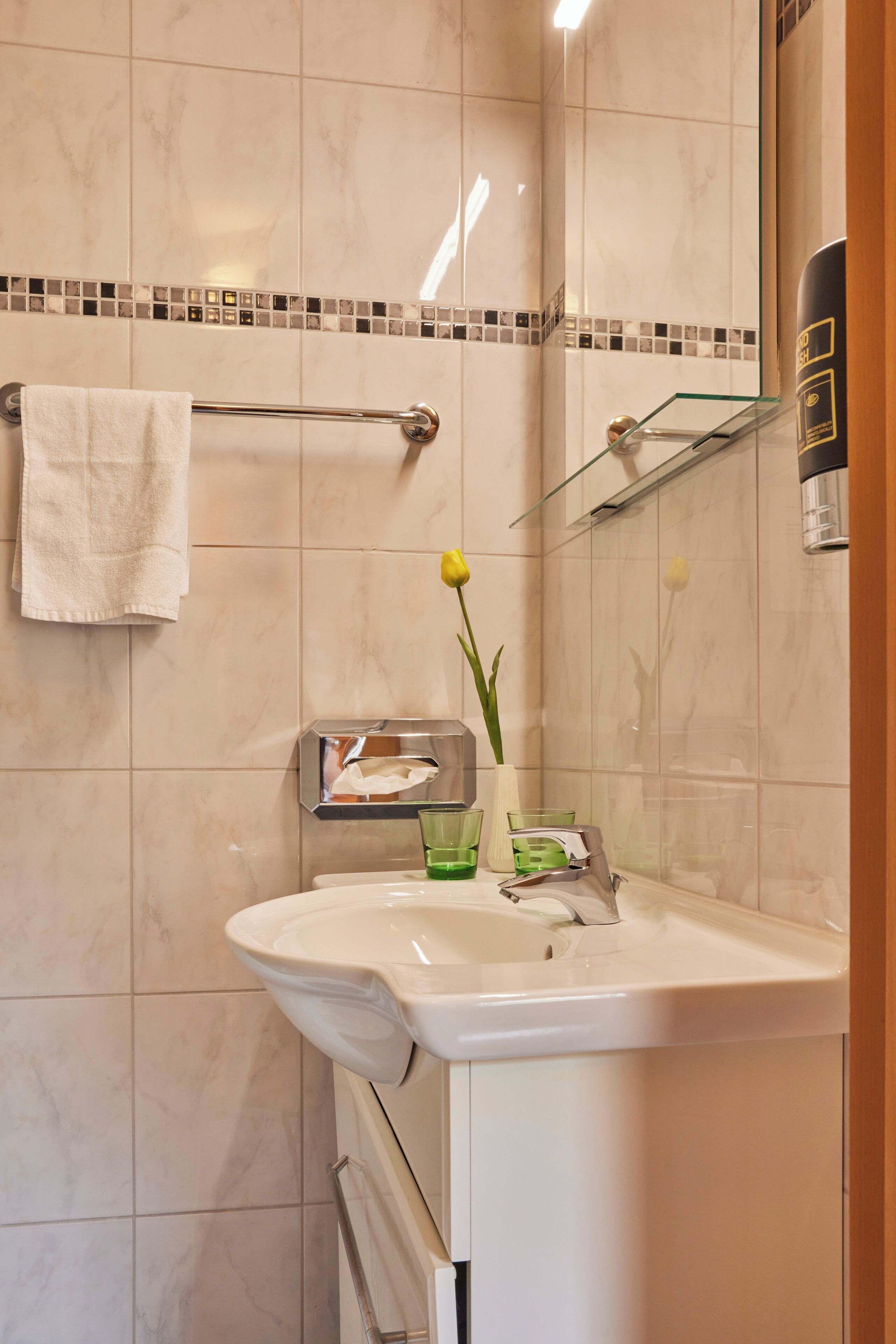 A bathroom with a white sink, a glass shelf, a towel rack, and a mirror.