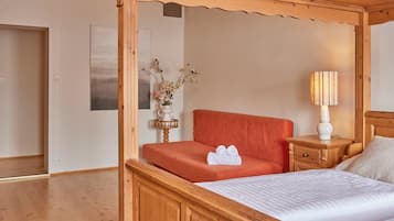 Un dormitorio con cama con dosel, una mesita de noche con lámpara, un jarrón con flores y un cuadro en la pared.