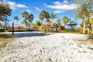 A sandy beach area with palm trees, a playground, and a gazebo.