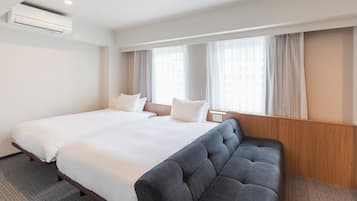 A hotel room with a large bed, a sofa, a window with curtains, and an air conditioning unit.