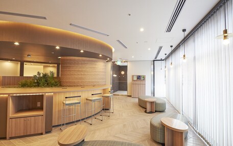 A modern reception area with a curved wooden counter, bar stools, and a seating area with round tables.