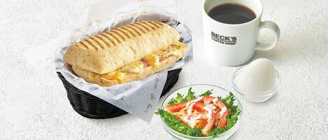 A sandwich in a basket, a cup of coffee, and a salad bowl.