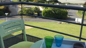 Un balcon donnant sur la plage, une chaise avec un coussin et une table sur laquelle se trouve un plateau avec des verres et un livre intitulé « BRASSERIE DE LA PLAGE ».