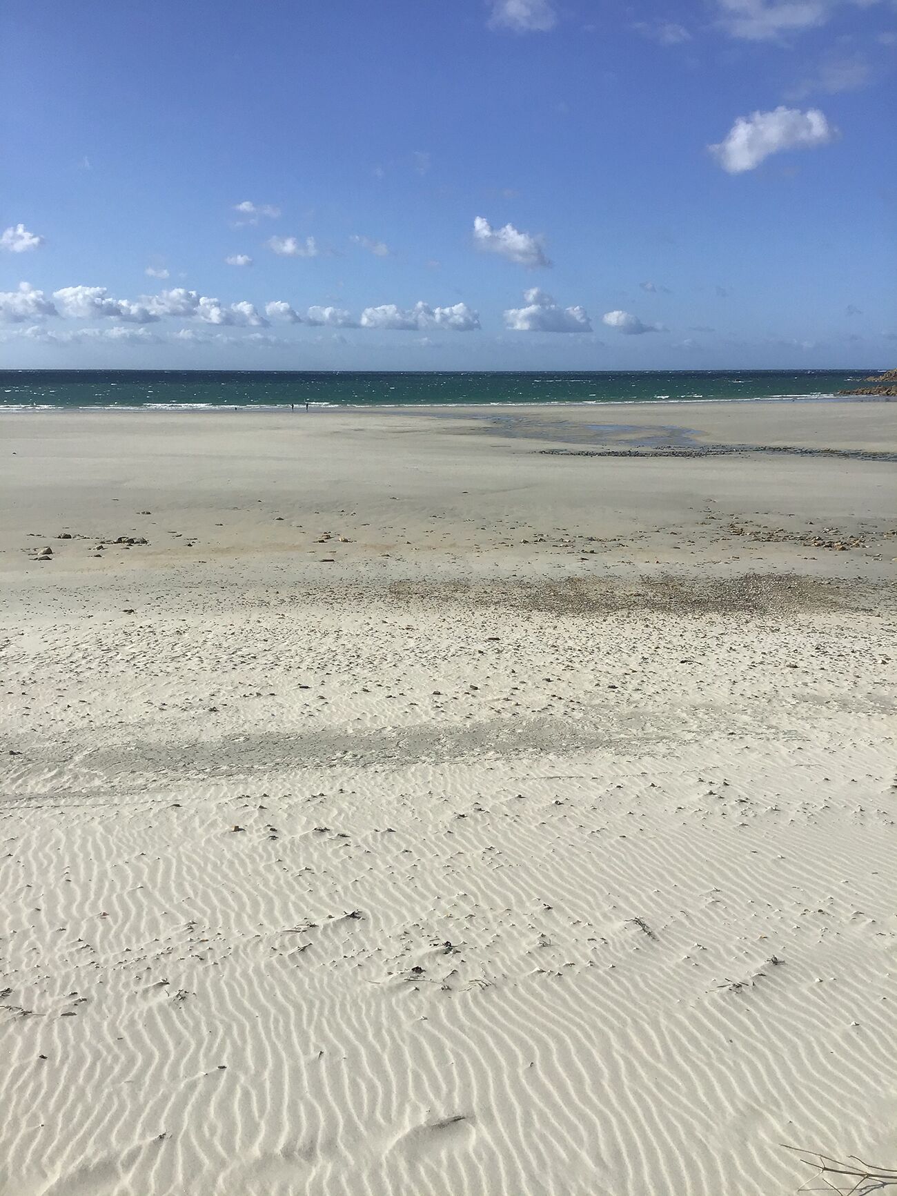 Ein sandiger Strand mit sanften Wellen und einem klaren Himmel.