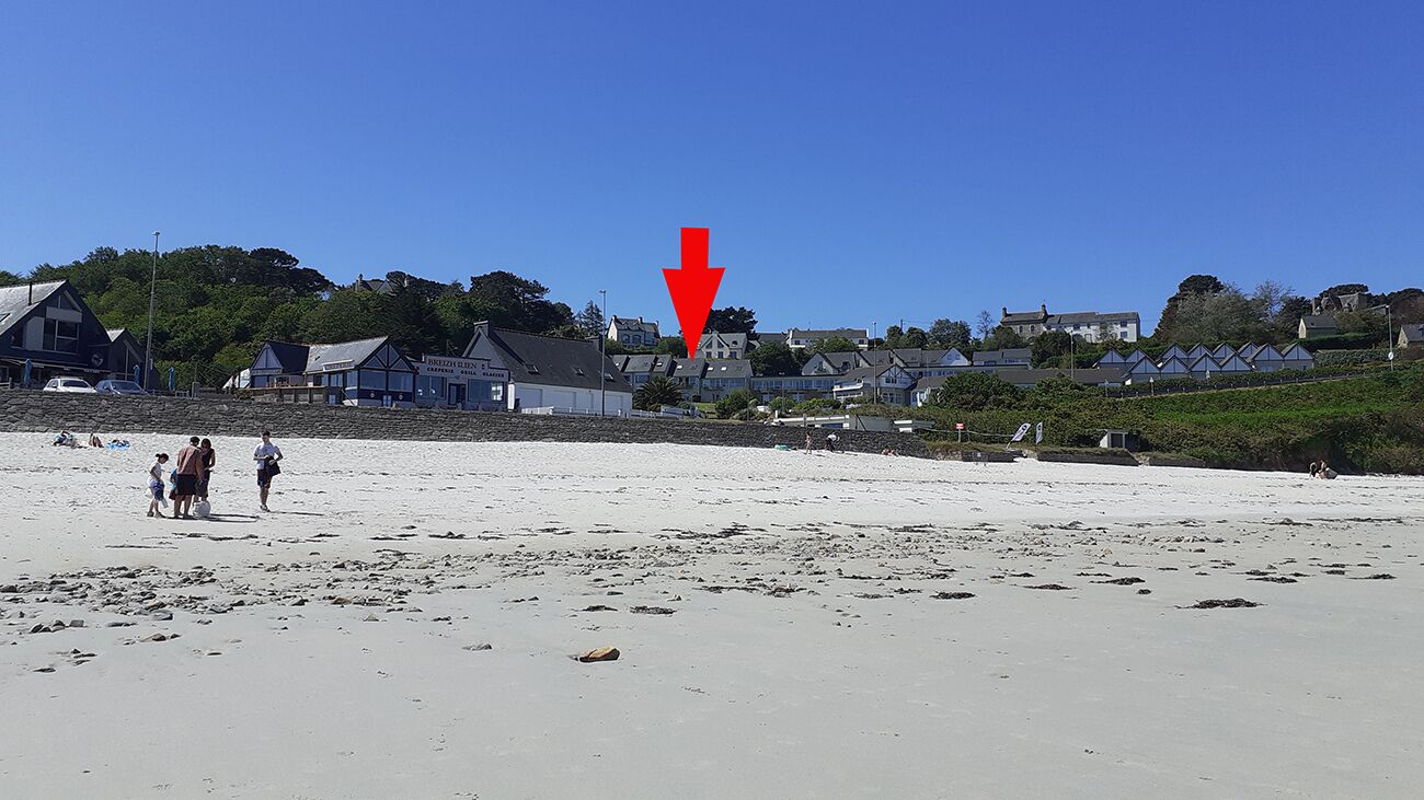A beach with houses in the background and a red arrow pointing downwards.