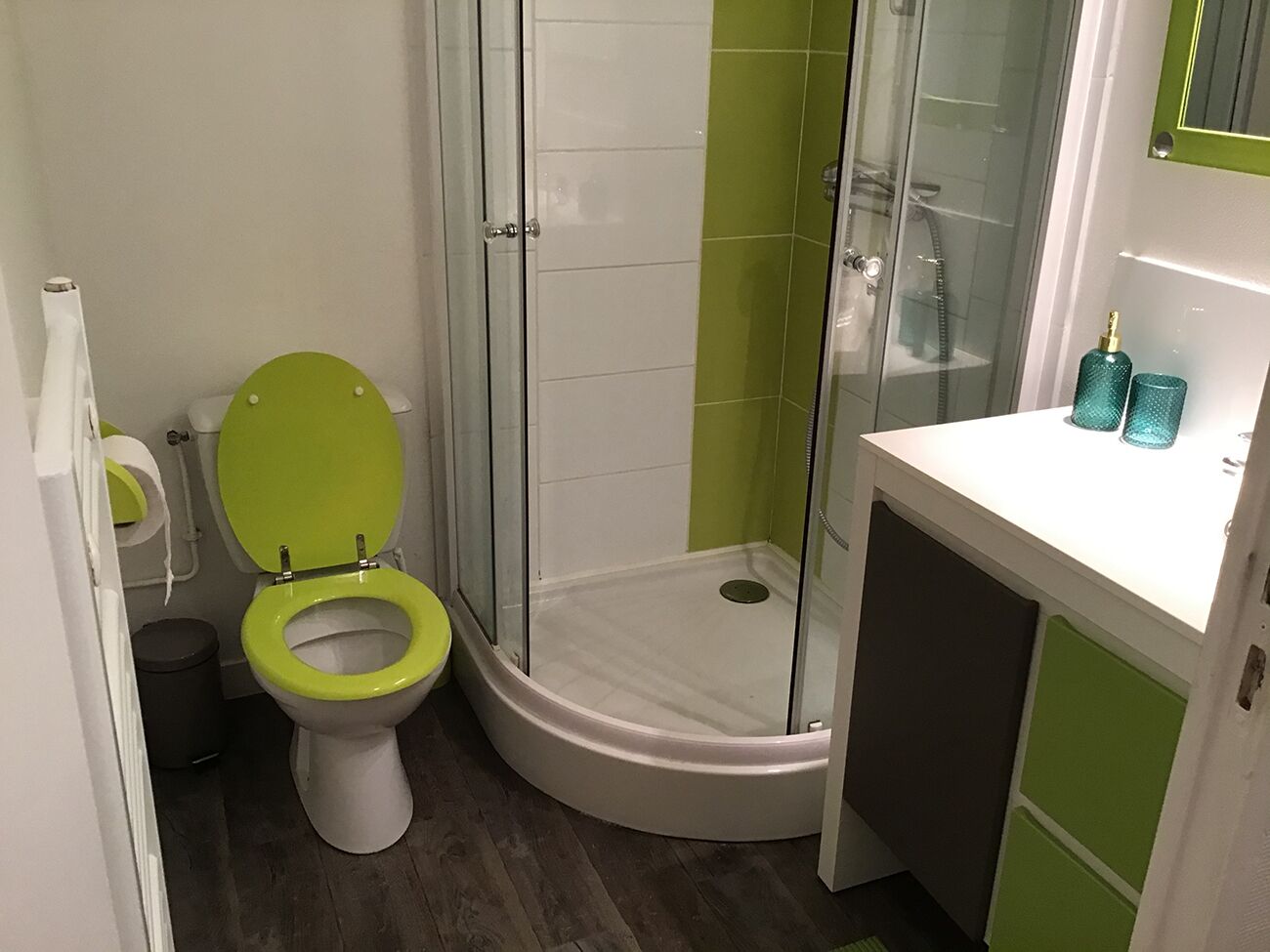 A bathroom with a green toilet, a glass-enclosed shower, and a white sink with green cabinets.
