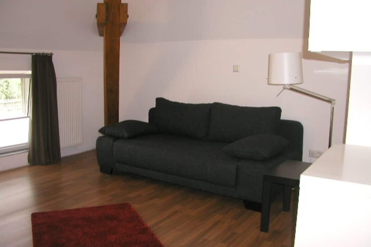 A living room with a dark grey sofa, a red rug, a wooden floor, a white desk, and a lamp.