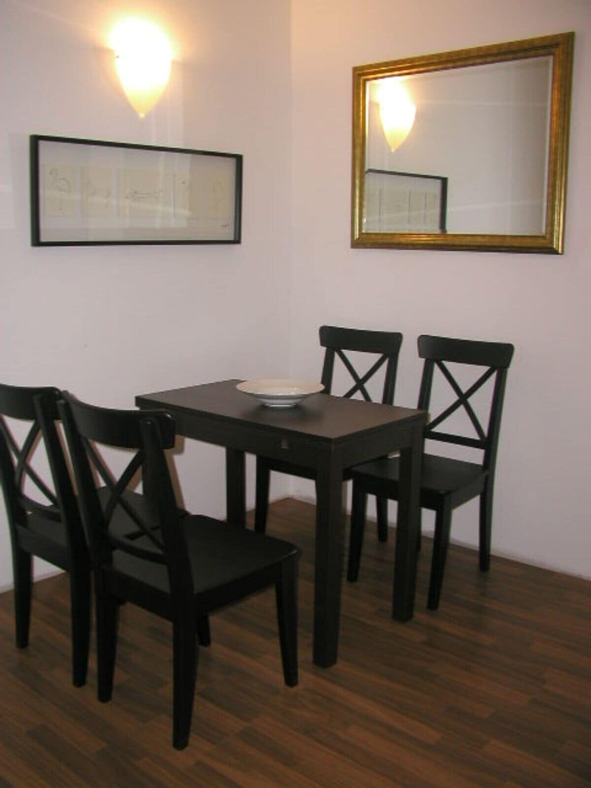 Een eetruimte met een donker houten tafel en vier stoelen, een inlijsting foto aan de muur, en een spiegel met een gouden lijst.