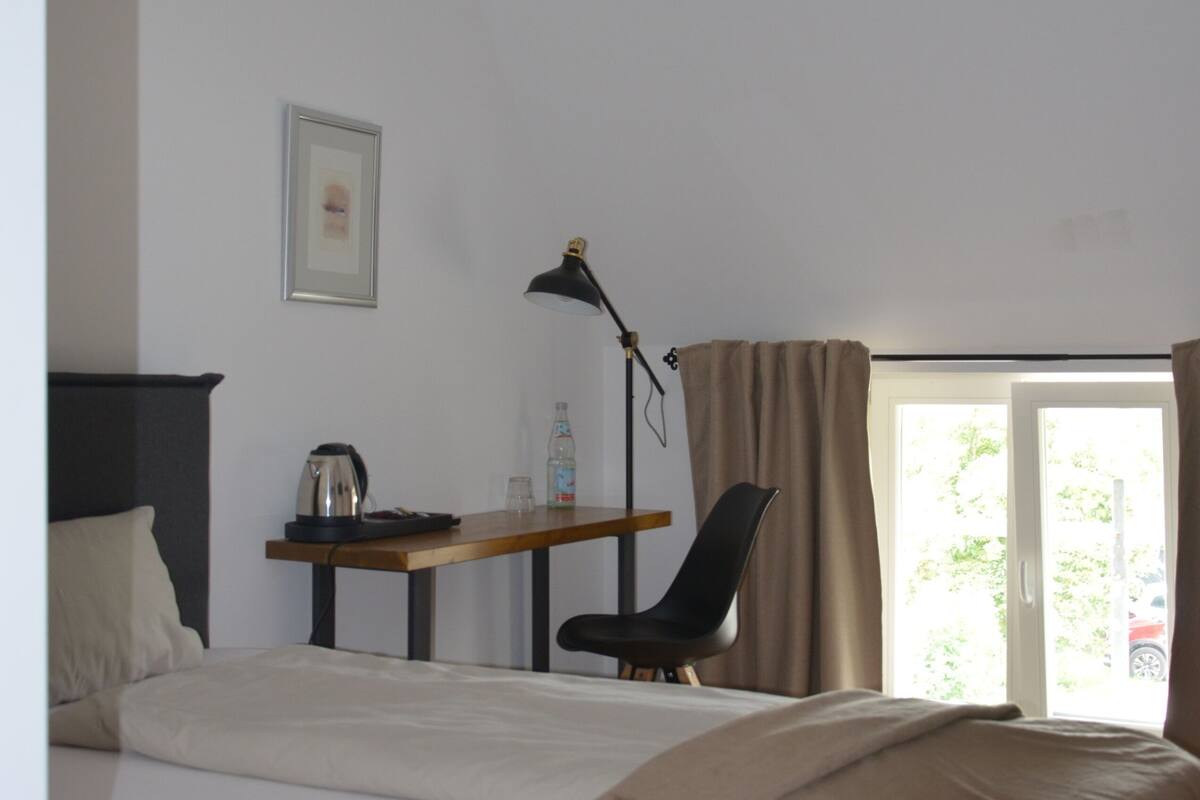 A bedroom with a bed, a desk, a chair, a lamp, and a window with curtains.