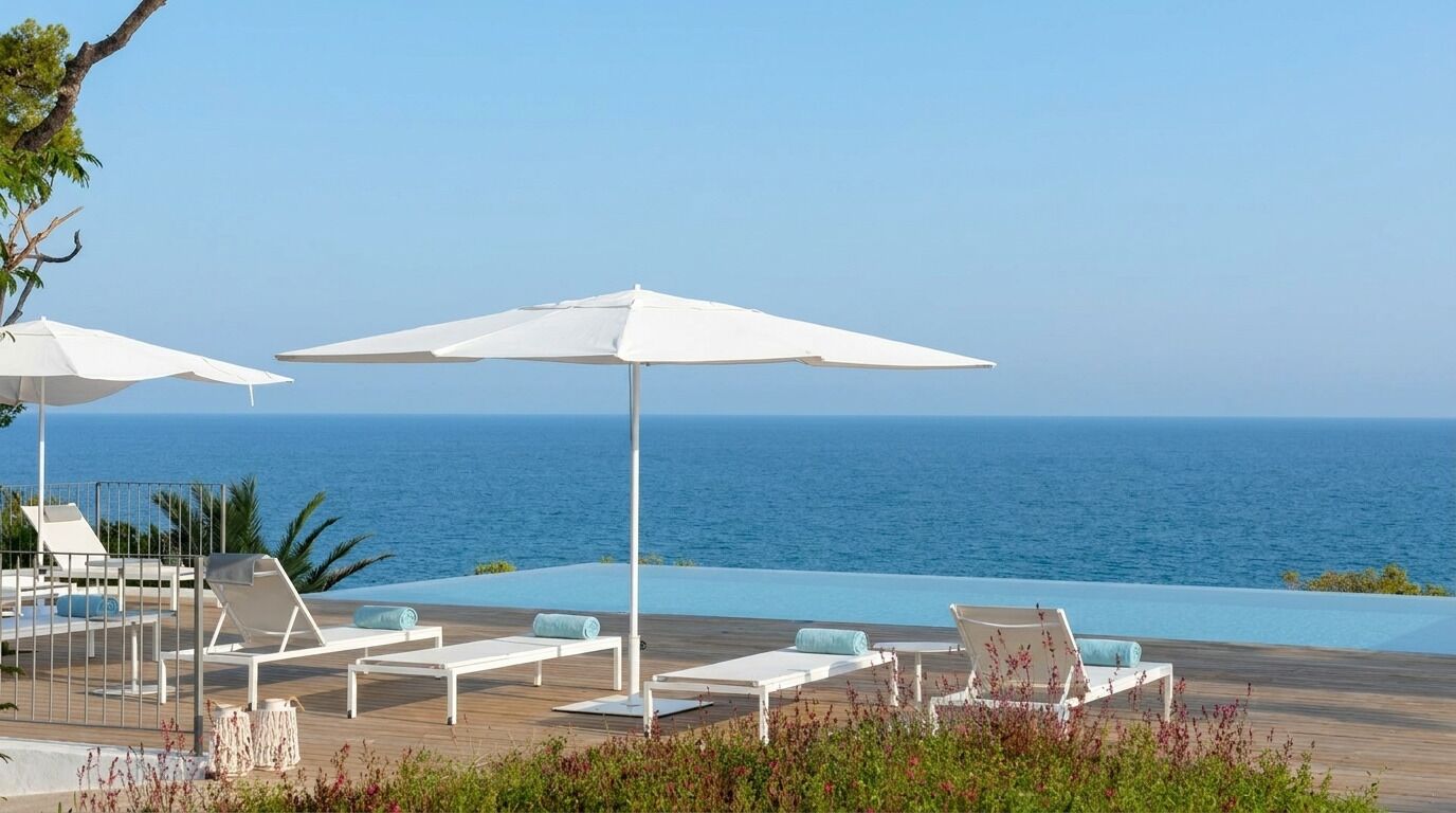 Zona junto a la piscina con sillas de descanso blancas y sombrillas, con vista al mar.