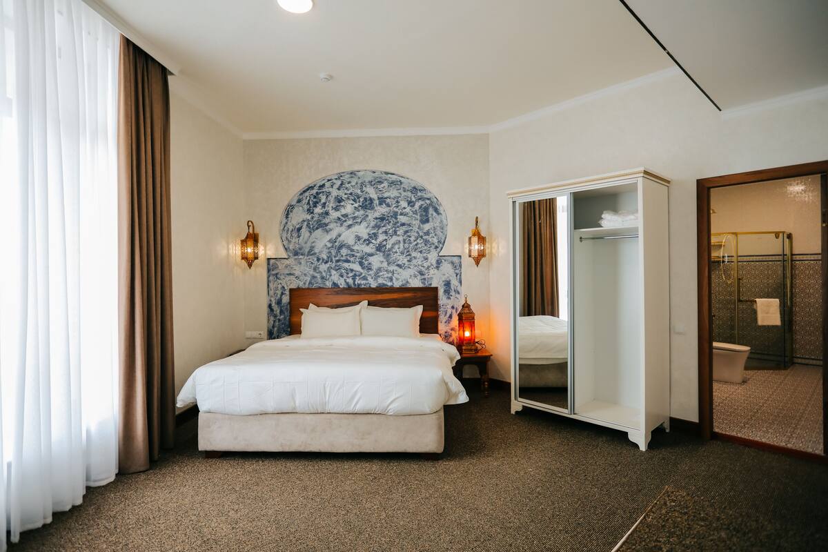 A hotel room with a large bed, a wardrobe, a mirror, and a nightstand with a lamp.