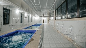 Un largo pasillo con una hilera de sillas transparentes a un lado y un área de spa con dos tinas de hidromasaje al otro.