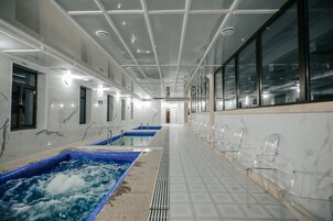 Un largo pasillo con una hilera de sillas transparentes a un lado y un área de spa con dos tinas de hidromasaje al otro.