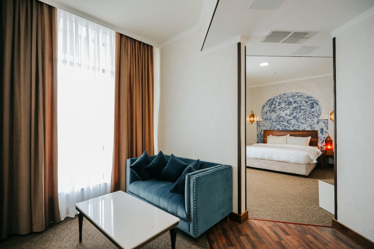 A hotel room with a large bed, a blue sofa, a white table, and a large mirror.