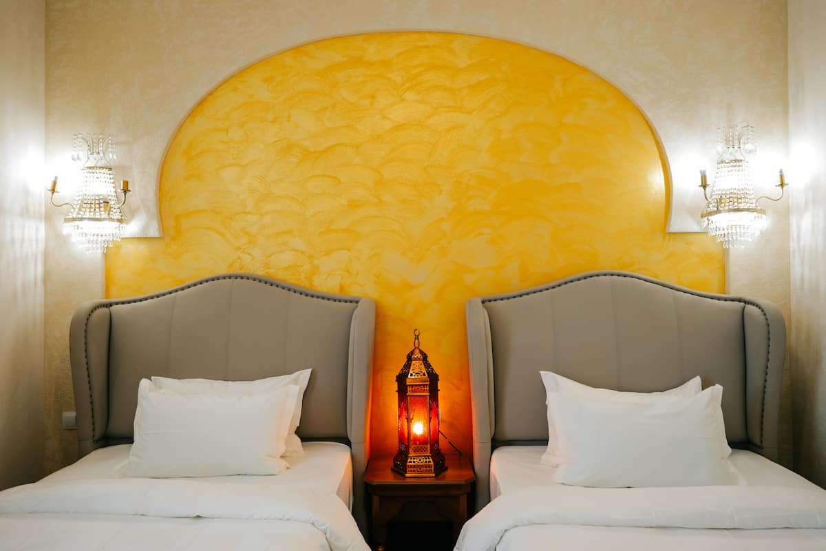 A hotel room with two beds, a large decorative wall, and wall-mounted lights.