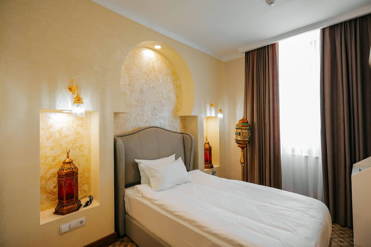 A hotel room with a large bed, two wall-mounted lamps, and a window with curtains.