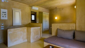 A room with a sofa, a coffee table, and a lamp. There is a door and a window in the background. - Sotiris Villas (Kefalonia)