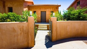 A building with a traditional architectural style, featuring a tiled roof and stucco walls. There is a set of steps leading to a door, flanked by low walls with greenery. - Sotiris Villas (Kefalonia)