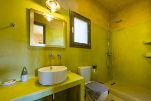 Un baño con pared amarilla, lavamanos blanco, espejo, ducha e inodoro.