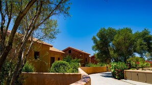 A courtyard with traditional buildings, a paved walkway, and lush greenery. - Sotiris Villas (Kefalonia)
