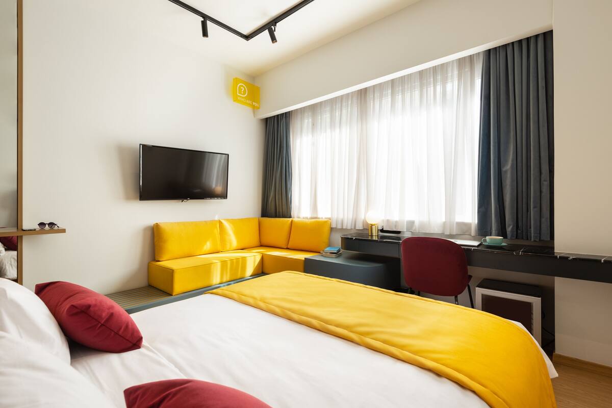 A hotel room with a bed, a desk, a chair, a TV, and a window with curtains.