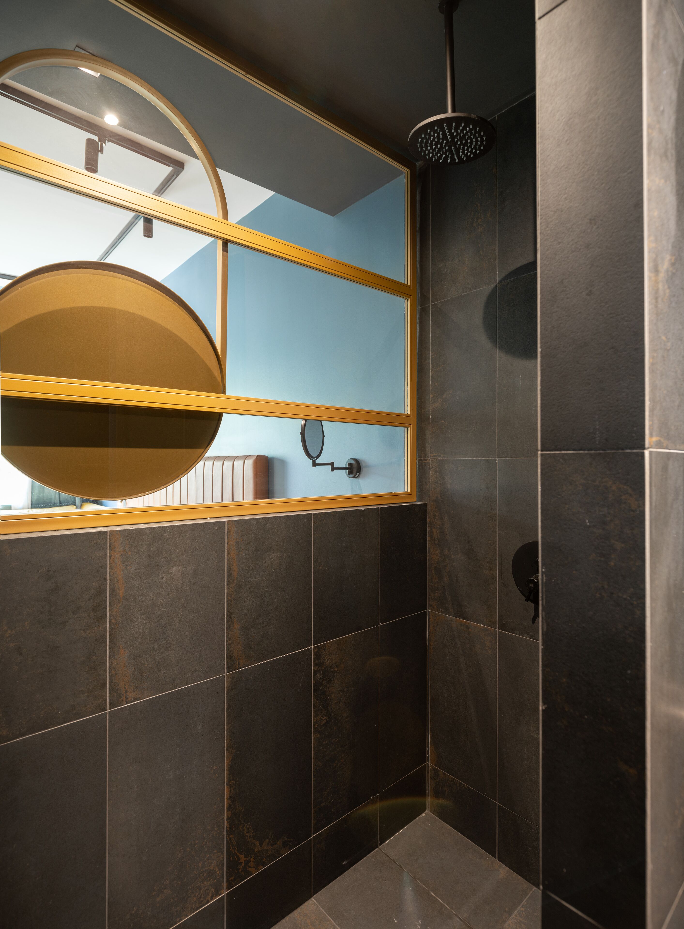 A modern bathroom with dark tiles, a round mirror, and a shower with a circular head.