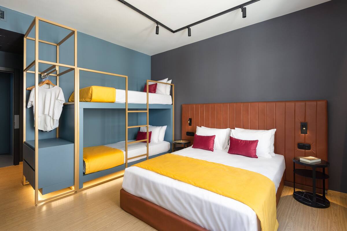 A hotel room with a bunk bed, a wooden wardrobe, a bedside table, and a nightstand.