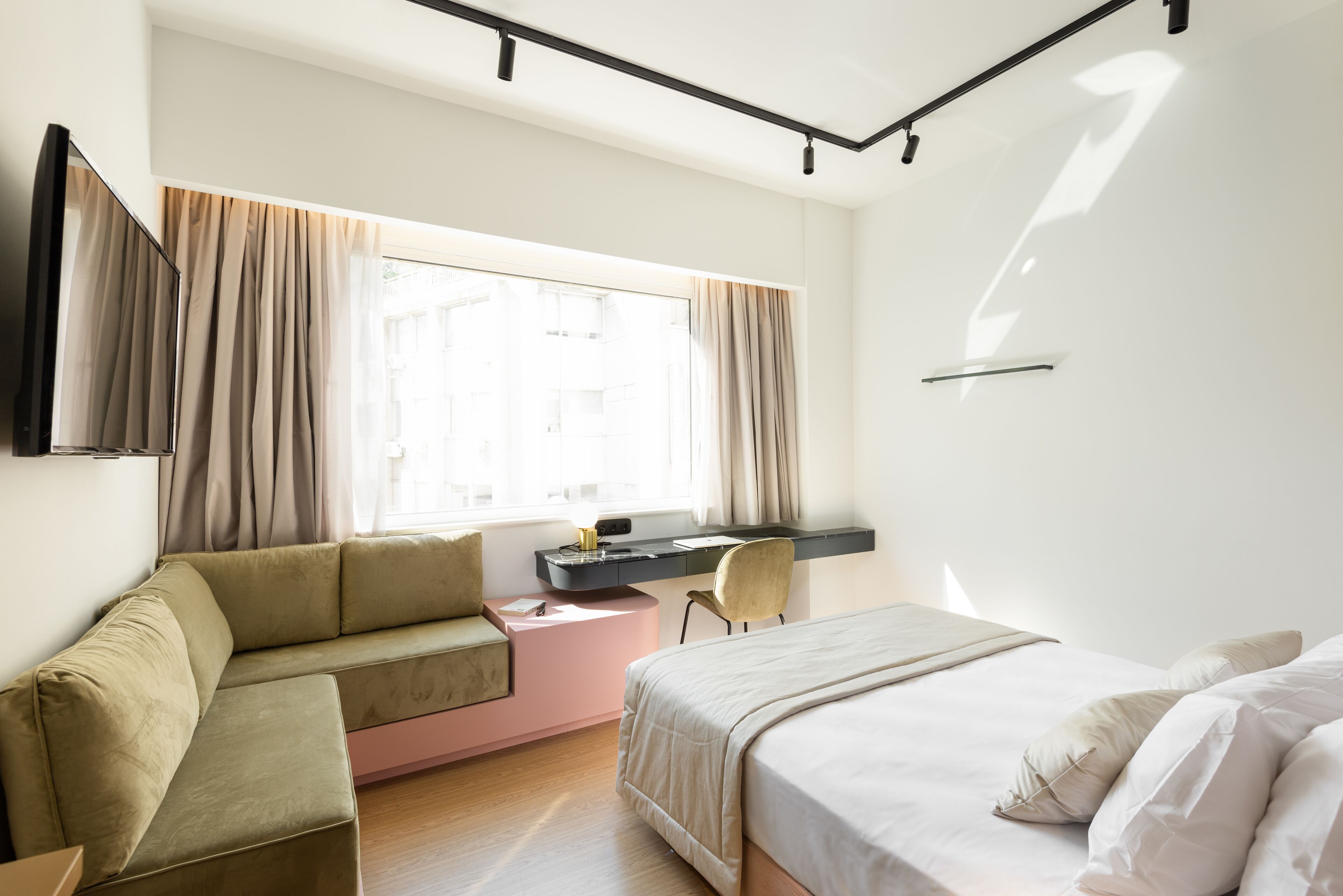 A modern hotel room with a bed, a sofa, a desk, and a chair.