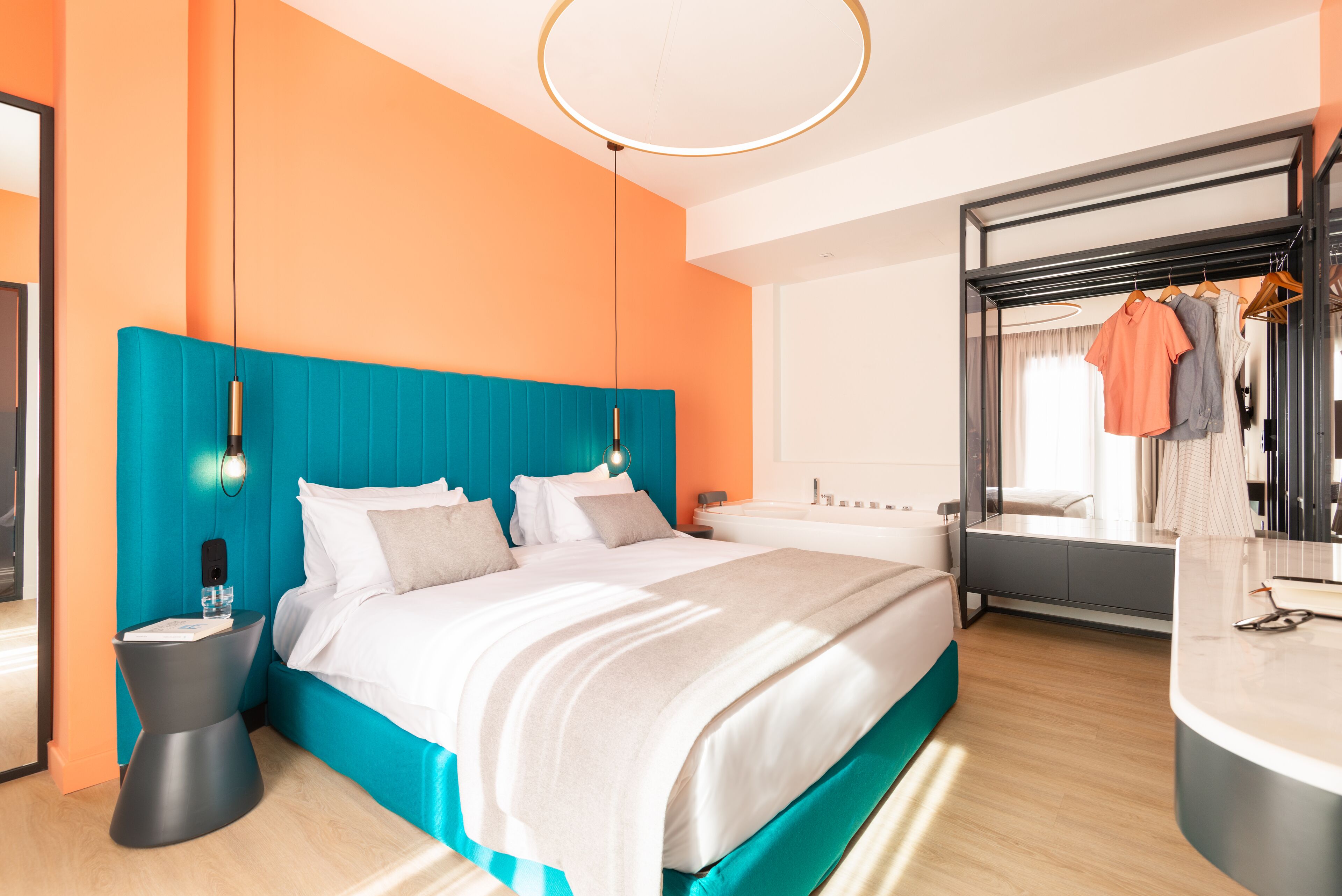Een moderne hotelkamer met een groot bed, een badkamer met bad en een kledingkast met daarin hangende kleding.