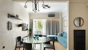 A modern living space with a round glass dining table, black chairs, a blue sofa, and a large window with curtains.