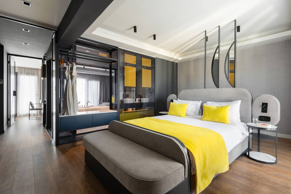 A modern hotel room with a large bed, a bench, a bedside table, and a built-in wardrobe.