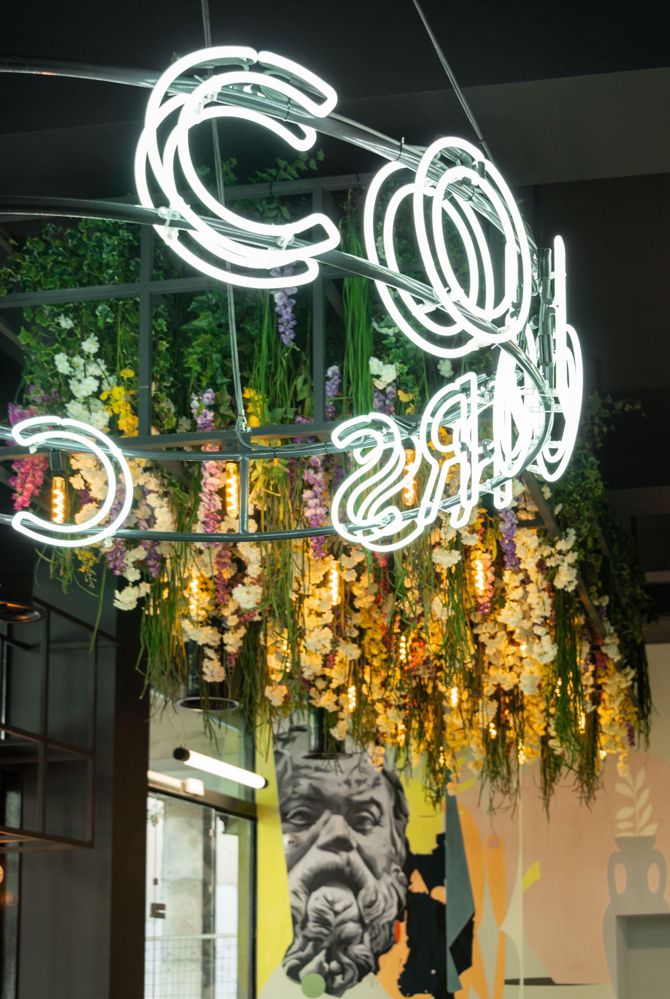 A neon sign with the letters "C" and "O" prominently displayed, surrounded by hanging floral arrangements.