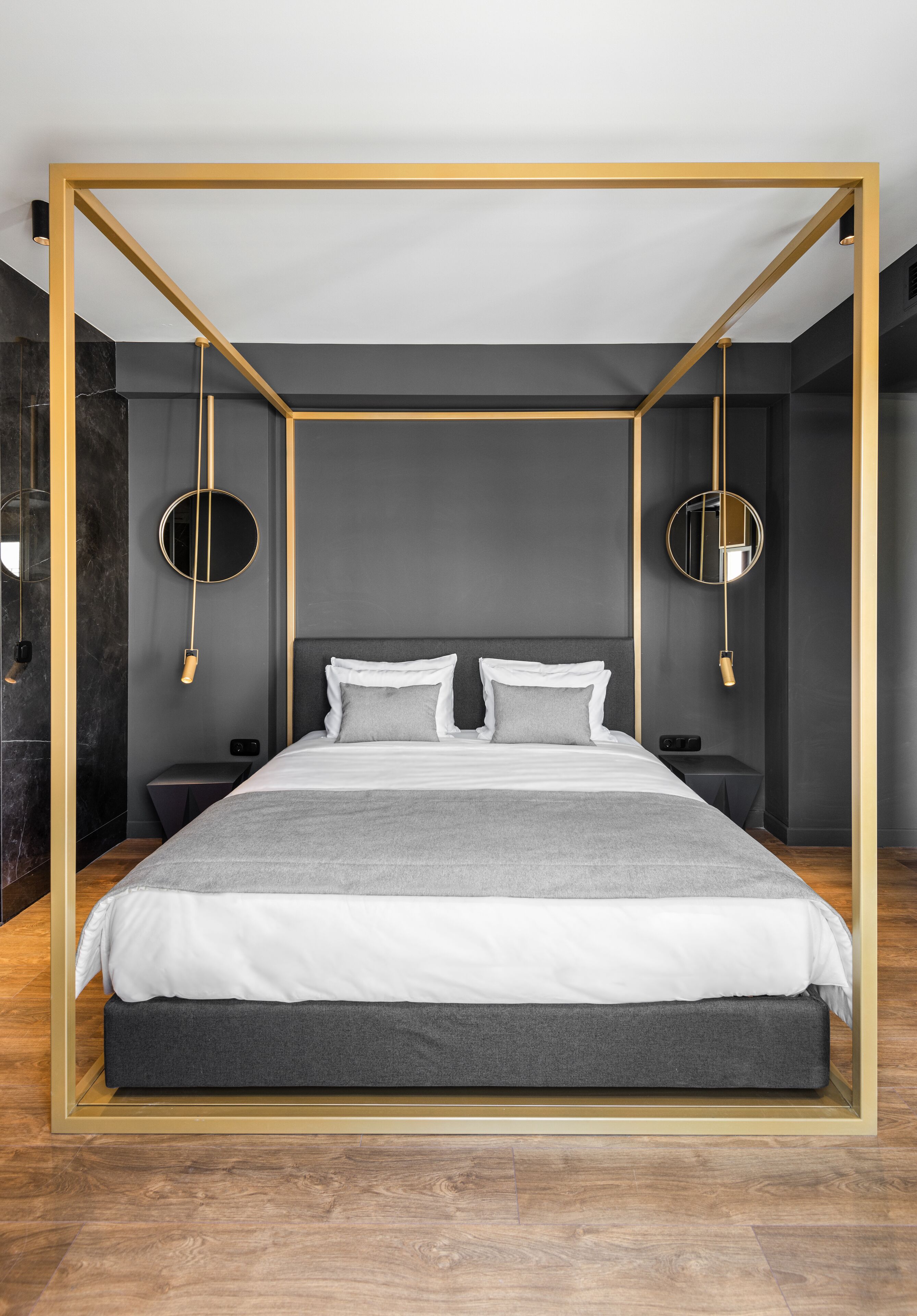 A modern bedroom with a minimalist design, featuring a bed with white bedding, two bedside tables, and a circular wall-mounted light fixture.