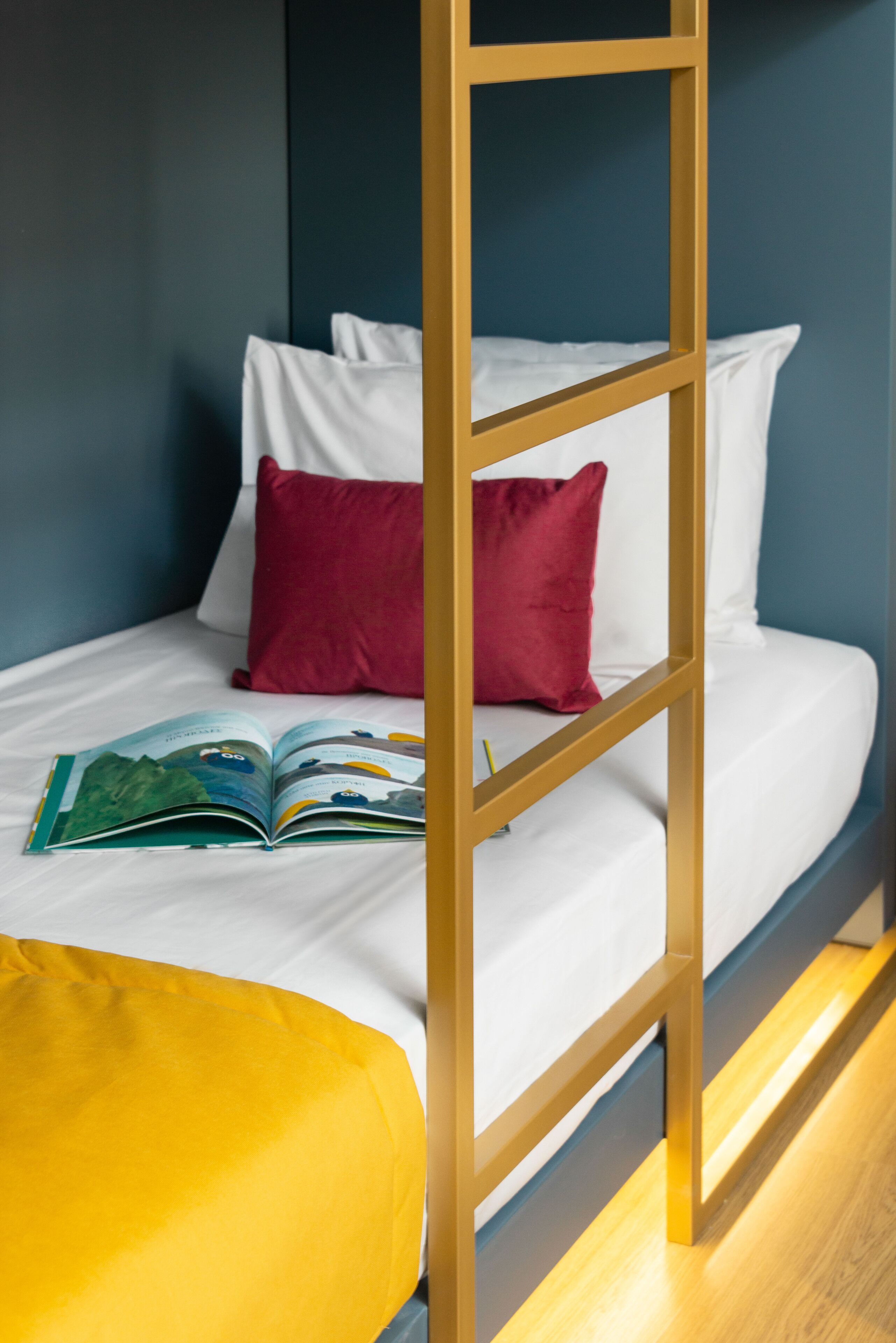 A bunk bed with white bedding and a red pillow, a yellow cushion, and a book on the lower bunk.