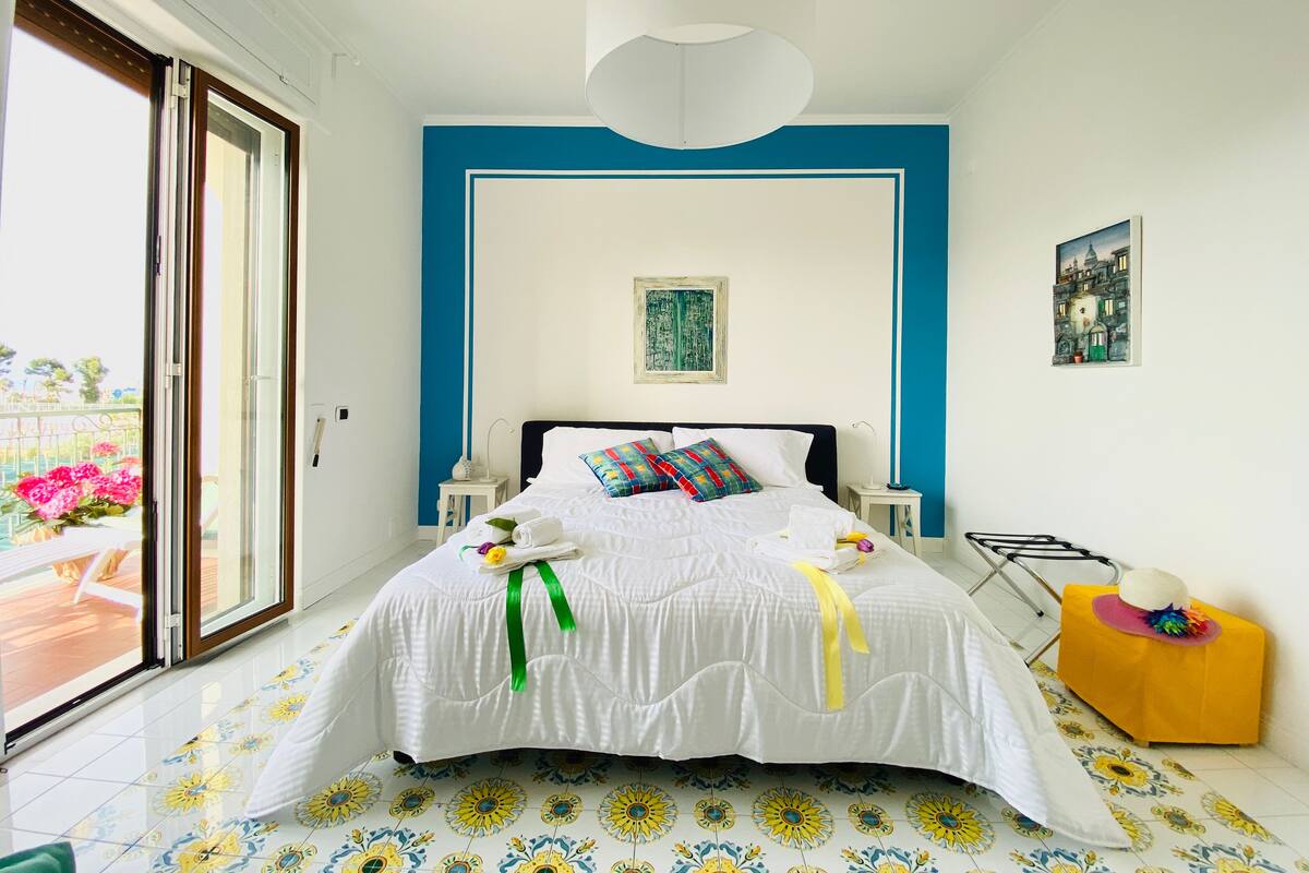 Ein Schlafzimmer mit einem Bett, einem Nachttisch, einem kleinen Tisch mit Hut und einem Gemälde an der Wand.