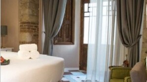 Une chambre d’hôtel avec un lit, un fauteuil vert, une porte en bois et une fenêtre avec des rideaux.