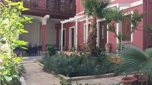 Un bâtiment à la façade rouge, doté d’un balcon et d’un jardin agrémenté de diverses plantes et d’un palmier.