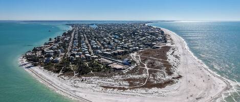 An aerial view of a coastal area with a densely packed residential zone, a sandy beach, and clear blue waters.