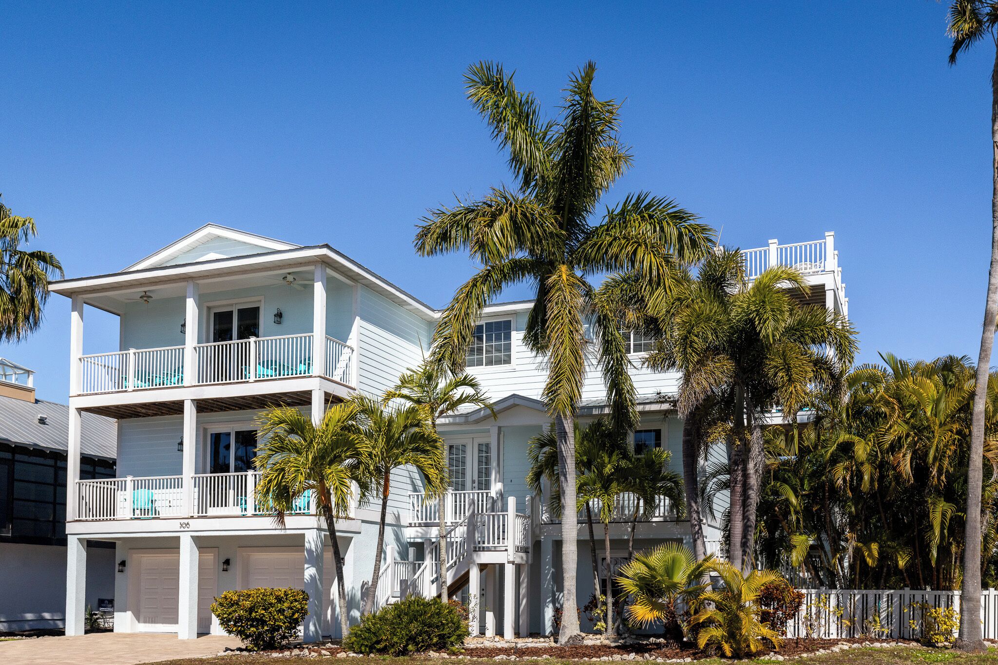 A two-story beachfront property with a white exterior, multiple balconies, and palm trees.