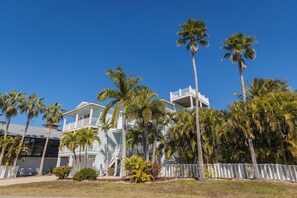 A multi-story building with a white exterior, surrounded by palm trees and a white fence. - Still Waters Beach House- A north end tropical getaway. (Anna Maria)
