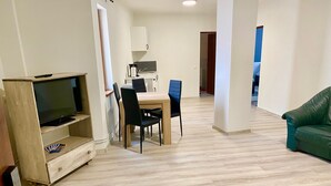 A living room with a TV, a dining table with chairs, a green sofa, and a kitchen area with cabinets and a sink. - Cardinal Central Apartment (Satu Mare)