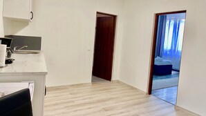 A modern, minimalistic hotel room with a wooden floor, a small kitchenette, and a view of the outdoors through a large window. - Cardinal Central Apartment (Satu Mare)
