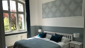 Un dormitorio con cama, dos mesitas de noche, una ventana con cortinas y una obra de arte colgada en la pared.
