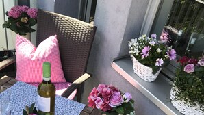 Un patio con mobiliario de mimbre, una mesa con mantel estampado y macetas con flores.