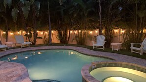 A swimming pool with a hot tub, surrounded by lounge chairs and palm trees.