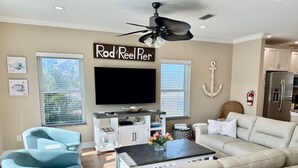 A living room with a beige sofa, a blue armchair, a coffee table, a flat-screen TV, and a ceiling fan.