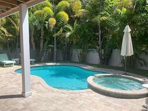 Piscina com hidromassagem, cercada por um pátio de tijolos e vegetação exuberante.