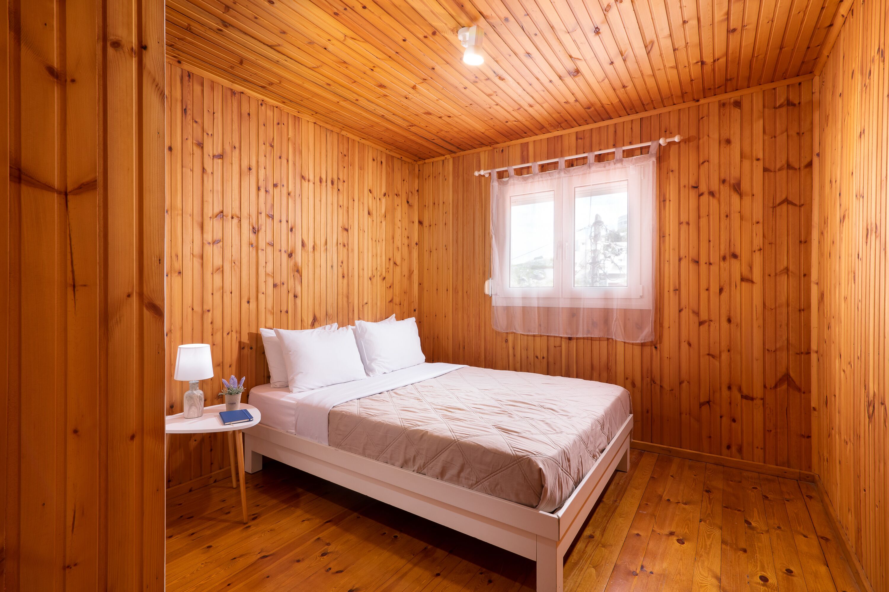 A wooden-paneled room with a bed, a nightstand, and a window with curtains.