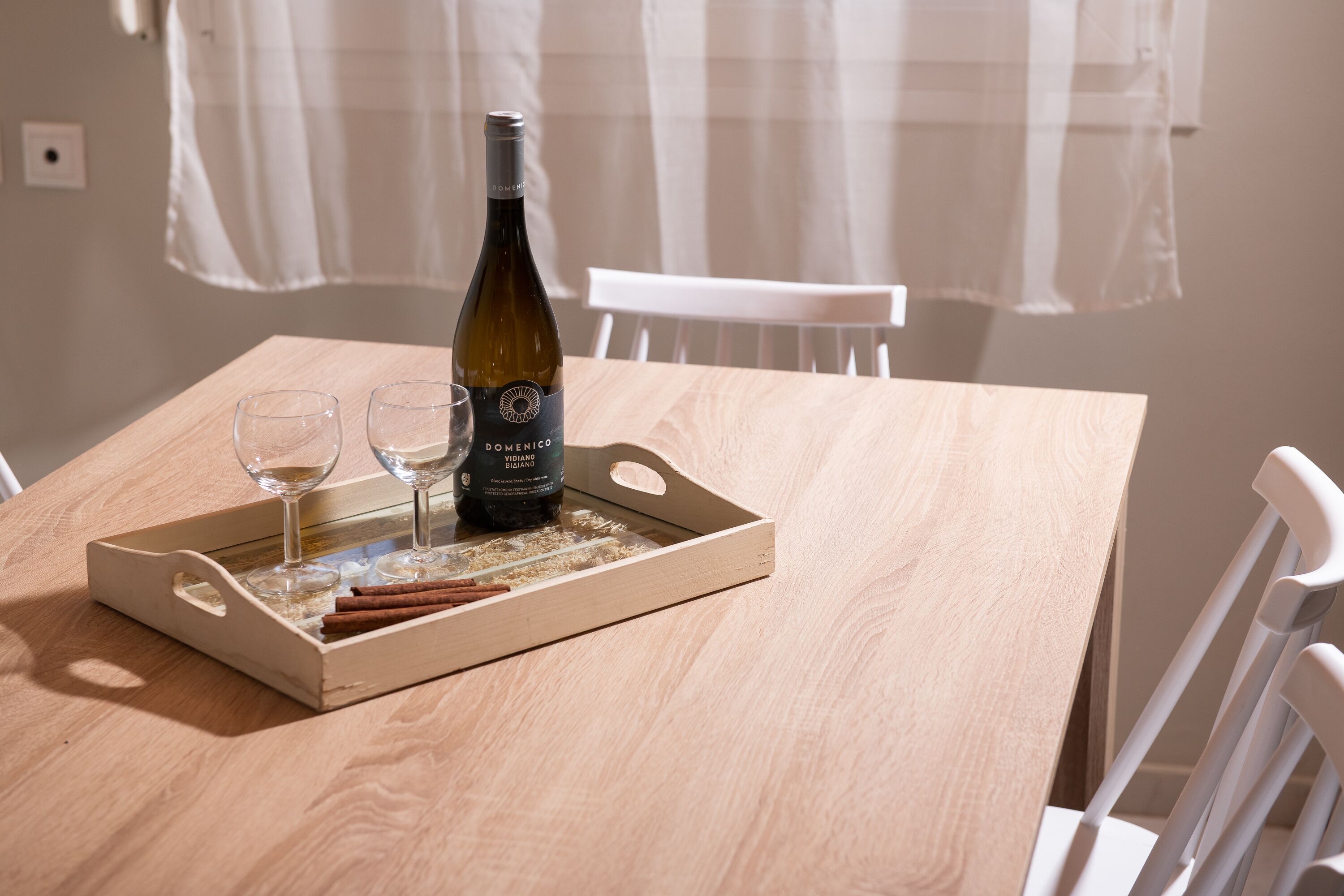 A wooden table with a bottle of wine, two glasses, and cinnamon sticks on a tray.